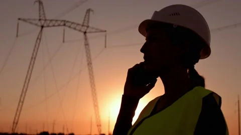 Electrical engineer in hardhat talking on the phone at sunset near the Stock Footage 204857753