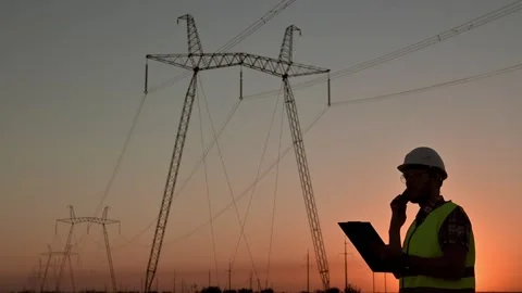 Electrical engineer in hardhat talking on the phone at sunset near the Stock Footage 208742609