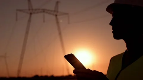 Electrical engineer in hardhat typing in phone at sunset near the electrical Stock Footage 201032156