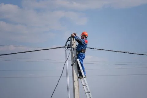 Electrical engineer performs wiring on a high pole standing on the stairs Stock Photos