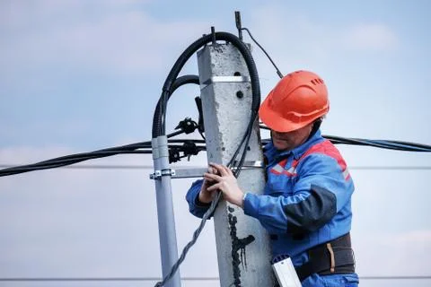 Electrical engineer performs wiring on a high pole standing on the stairs Stock Photos