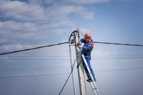 Electrical engineer performs wiring on a high pole standing on the stairs Stock Photos