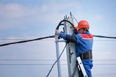 Electrical engineer performs wiring on a high pole standing on the stairs Stock Photos