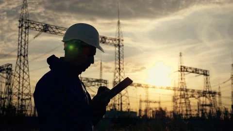 An electrical engineer wearing a helmet works with a tablet near high voltage Video stock 138596176