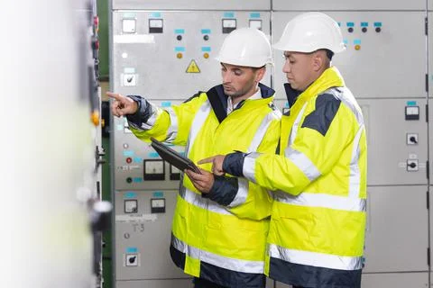 Electrical engineers checking control panel board with tablet. High voltage Foto stock