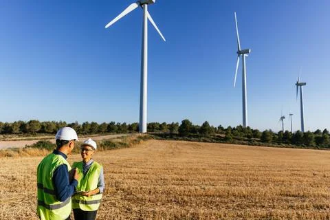 Electrical engineers inspect a wind power plant wearing reflective vests and Stock Photos