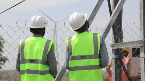 Electrical engineers observing wind turbine operation through a security fence Stock Footage 336394127