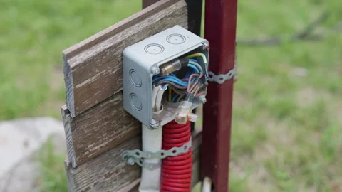 Electrical junction box with visible wiring and red conduit attached to wooden Stock Footage 340275233