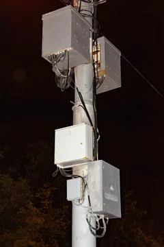 Electrical junction boxes with wires mounted on a grey utility pole at night Stock Photos