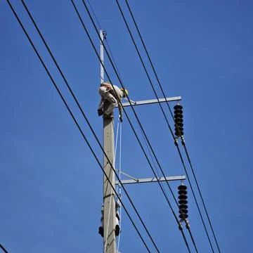 Electrical lineman worker climbing concrete power pole. Stock Photos