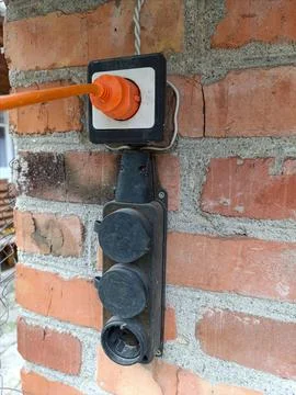 An electrical outlet on a brick wall with an orange cord attached to it Stock Photos