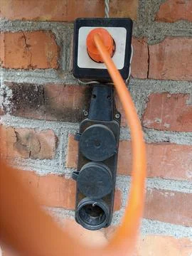 An electrical outlet on a brick wall with an orange cord 스톡 사진