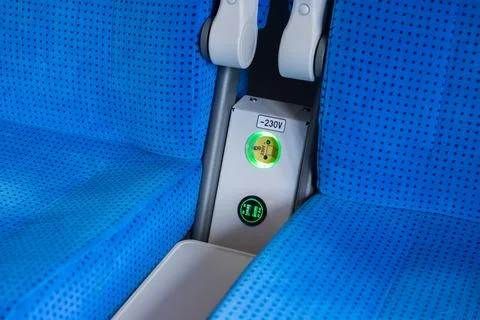Electrical power socket and USB charging ports between bright blue train seats Stock Photos