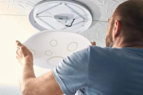 Electrical technician changes the LED lamp on the ceiling, saving electricity Stock Photos