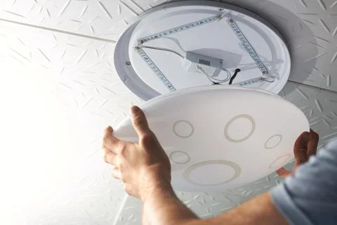 An electrical technician changes a low-consumption LED lamp into a residentia Stock Photos