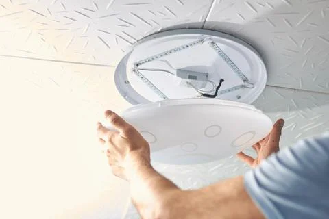 An electrical technician changes a low-consumption LED lamp into a residentia Stock Photos