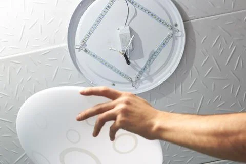 An electrical technician changes a low-consumption LED lamp into a residentia Stock Photos