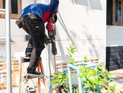 An electrical technician standing on a stepladder, using a heavy-duty demol.. Фото