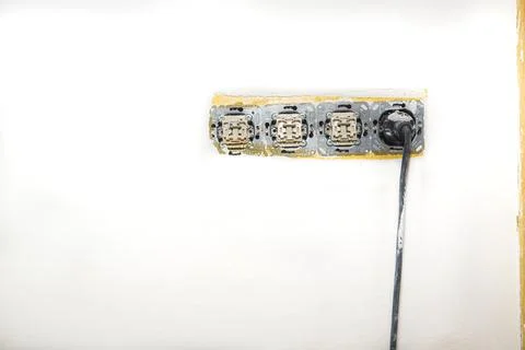 Electrical wire and opened plug socket on the old plastering wall. Stock Photos
