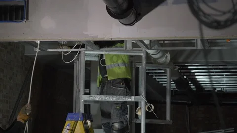 Electrican Pulling Wires With Workmate Through Industrial Ceiling Stock Footage 92700963