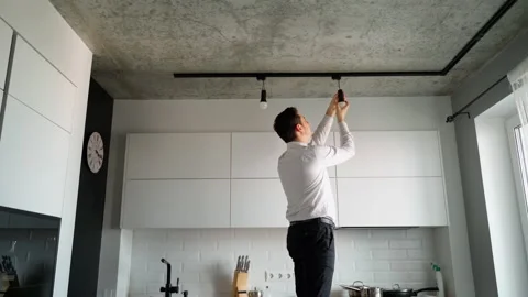 Electrician 30s man changing a light bulb in a modern white kitchen Stock Footage 153290470