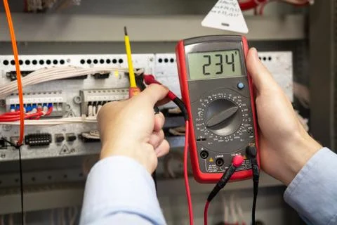 Electrician adjusts electrical control panel on power station, using tester. Foto stock