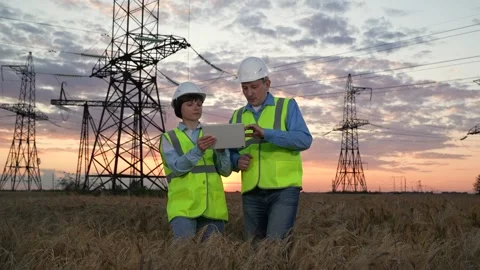 Electrician check tablet and walk across field against power transmission lines Stock Footage 280946028