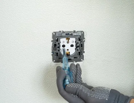 Electrician hands check current in socket using indicator screwdriver. Outlet Stock Photos