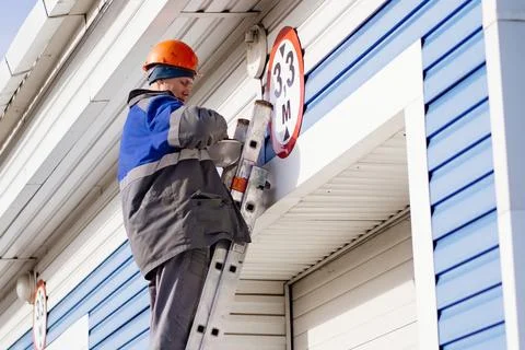 Electrician in hard hat changes light bulb in ceiling lamp outside industrial Stock Photos
