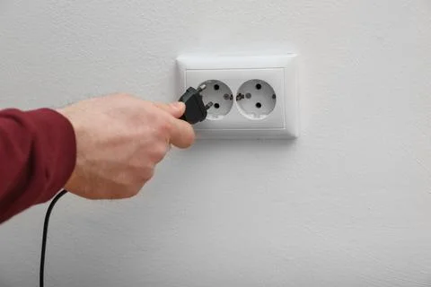 Electrician inserting plug into power socket on white background, closeup Stock Photos