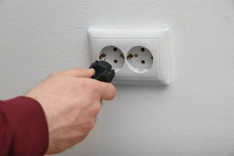 Electrician inserting plug into power socket on white background, closeup Stock Photos