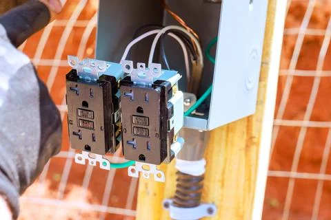 Electrician installing dual electrical outlets in circuit box located outdoors 写真素材