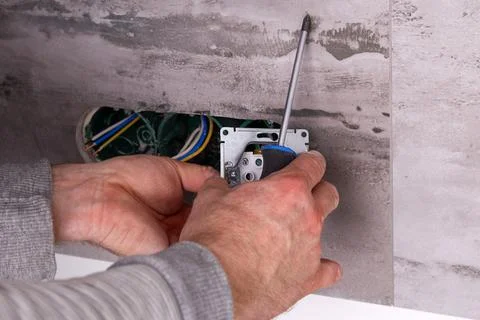 Electrician installing electrical outlets in a wall made of porcelain tiles. Stock Photos
