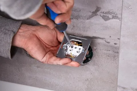 Electrician installing electrical outlets in a wall made of porcelain tiles. Stock Photos