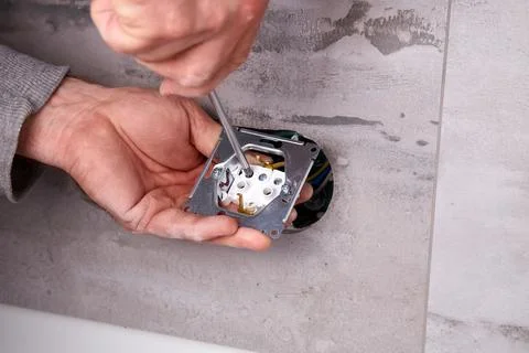 Electrician installing electrical outlets in a wall made of porcelain tiles. Stock Photos