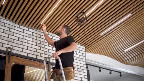 An electrician installs LED lamps on a wooden plank ceiling in a loft interior Stock Footage