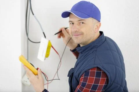 Electrician measuring voltage of cable on ceiling indoors Stock Photos