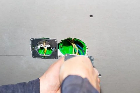 The electrician plugs electrical outlets into the socket boxes in the drywall Фото