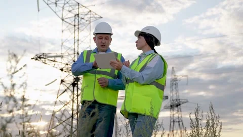 Electrician shows report on tablet to engineer walking across substation Stock Footage 255319763