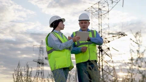 Electrician shows report on tablet to engineer walking across substation Stock Footage 257178686