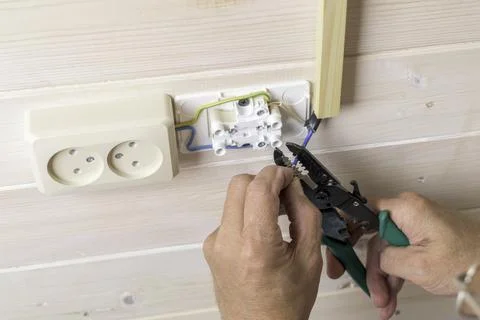 Electrician strips wire insulation while installing double wall socket on lig Stock Photos