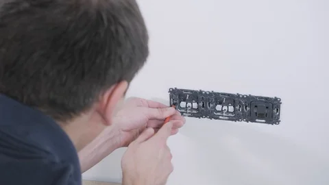 Electrician unscrews light switch basis from white wall Stock Footage 106377048