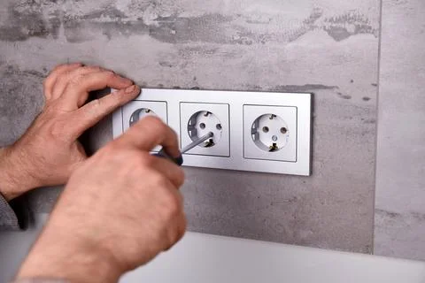 An electrician uses a screwdriver to install an electrical outlet on a wall.. Stock Photos