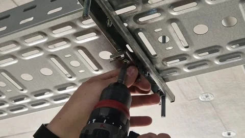 Electrician using power screwdriver to fix lamp mounting clip to cable tray Stock Footage 341426906