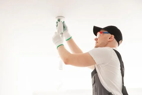 Electrician worker man assembling electric lamps in new apartment Stock Photos