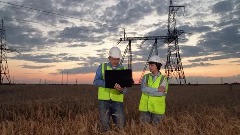 Electricians with laptop discuss innovative solution by power transmission lines Stock Footage 266940014