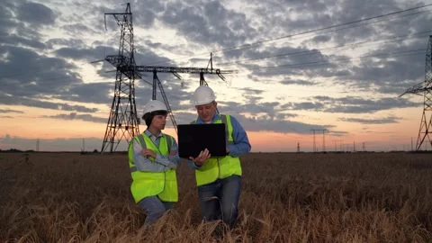 Electricians test network via laptop walking against power transmission lines Stock Footage 249028092