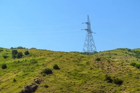 Electricity pylon rises above rolling green hills under bright blue sky Stock Photos