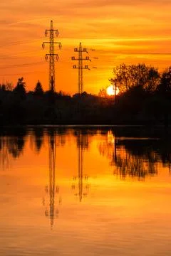 Electricity pylons on sunset background, reflection in a water. Stock Photos