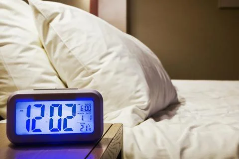 Electronic alarm clock stands on a bedside table in the room Stock Photos